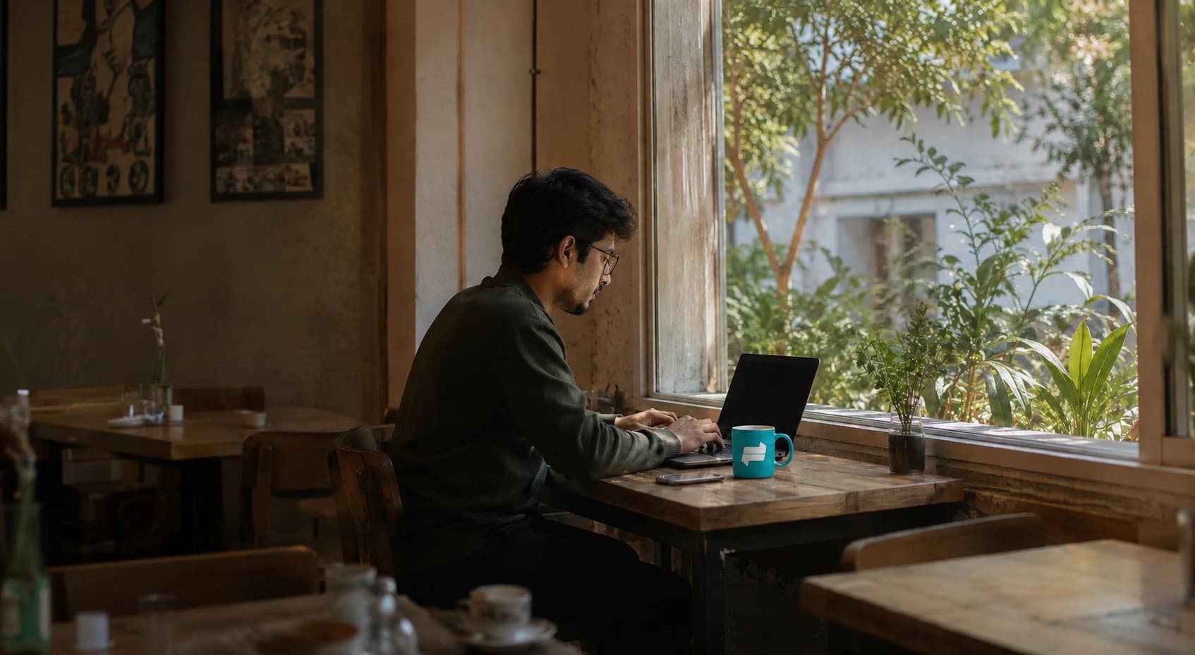Someone working on a laptop in a sunlit cafe, a Fazl mug beside them